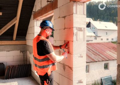 Murár pracuje na stene domu počas výstavby, kontroluje a upravuje tehlové murivo.