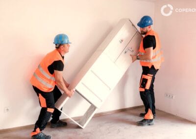 Dvaja pracovníci inštalujú elektrický rozvádzač na stenu.